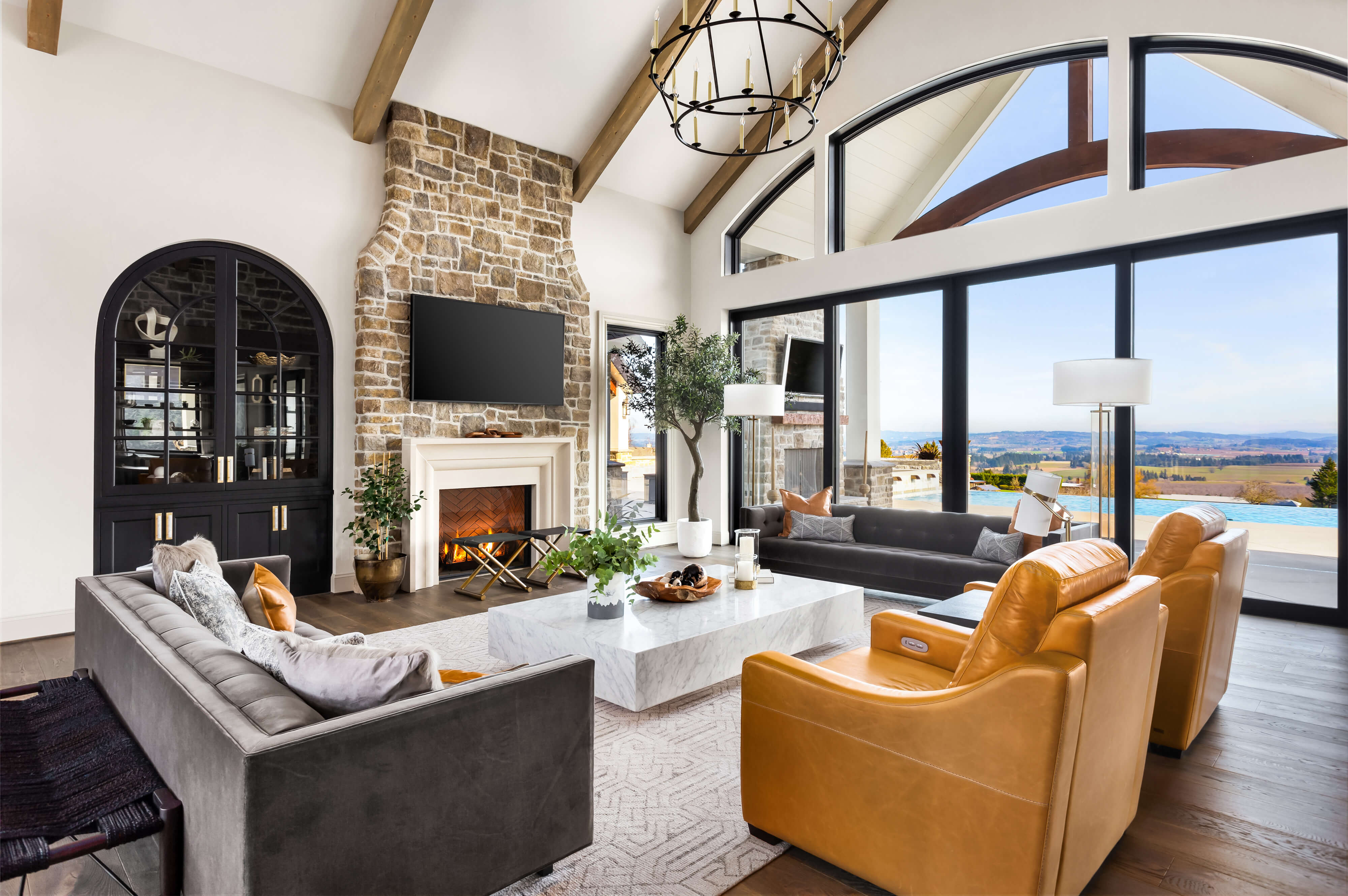 Beautiful living room in new modern  luxury home. Features vaulted ceilings, fireplace with roaring fire, and gorgeous exterior view with infinity pool and valley